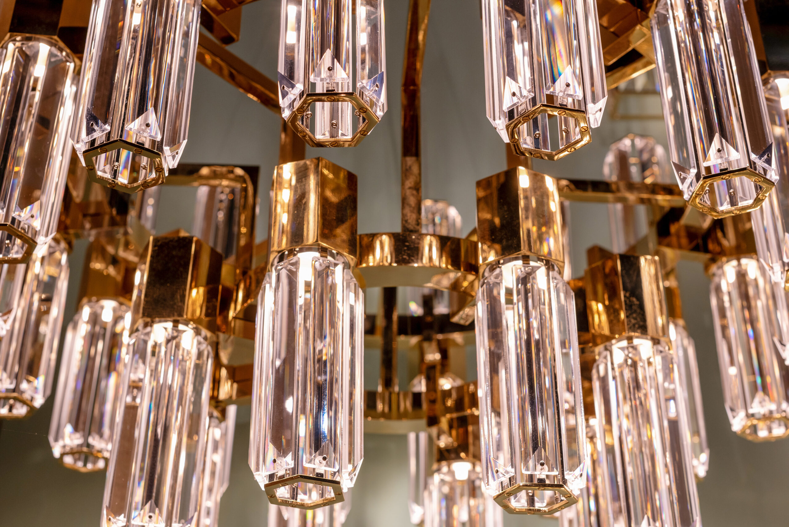 Close up on the stylish faceted glass prisms of a modern chandelier with gold or brass detail hanging from a ceiling in an interior decor concept