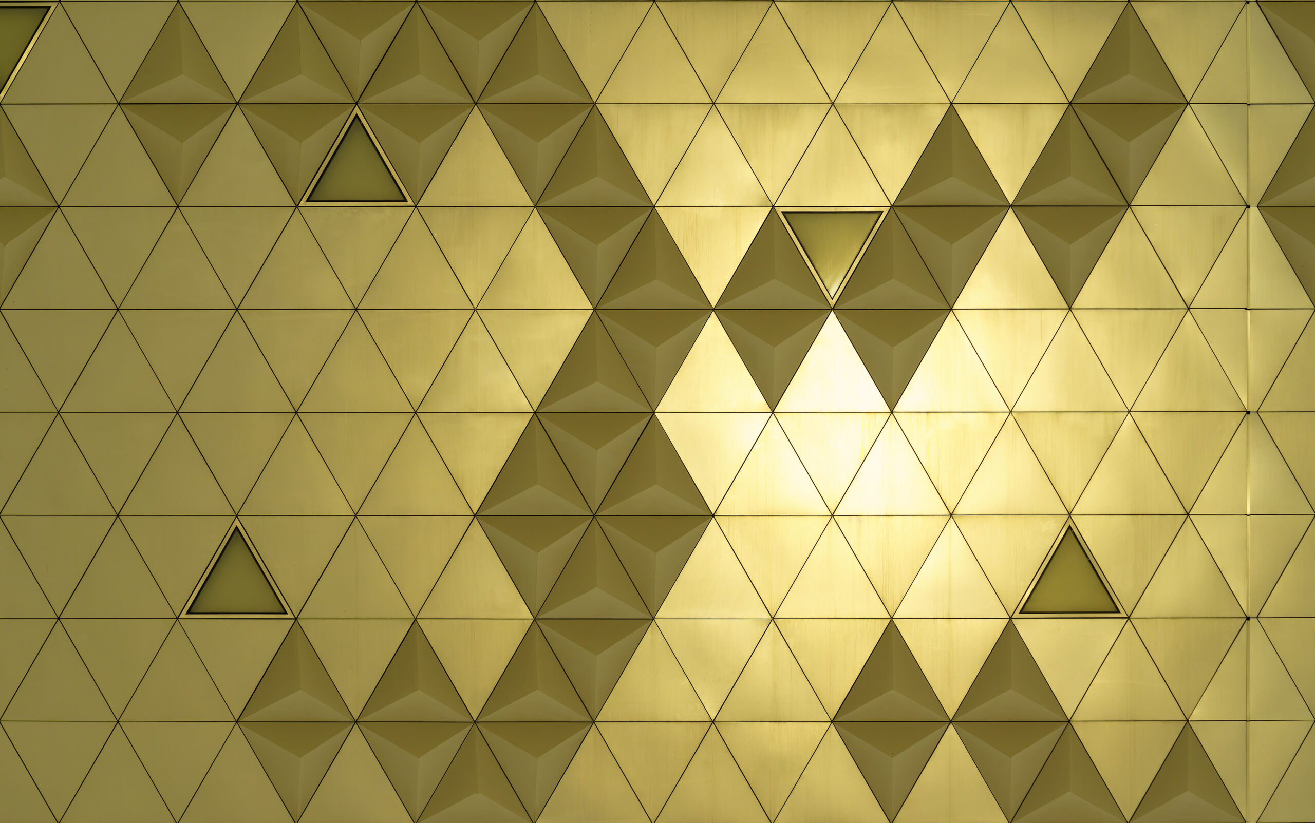 Golden diamond-shaped polished metal cladding panels of a modern building illuminated by sunlight. Abstract background for design.