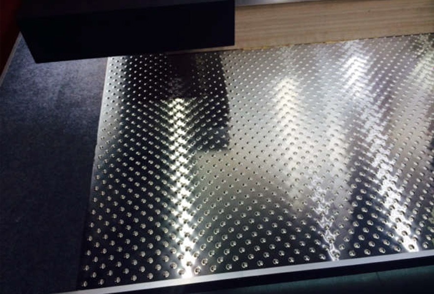 A close-up view of a metal sheet with a regular pattern of raised, round bumps reflecting overhead lights.