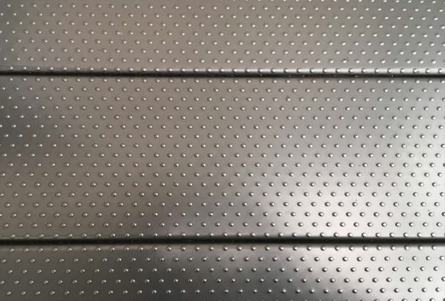 Close-up of a metallic surface with evenly spaced small raised dots and horizontal indentations separating sections, creating a textured and industrial pattern.