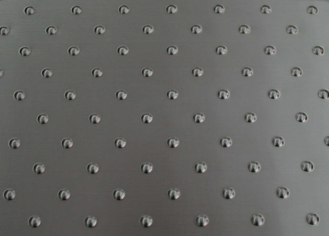 Close-up of a metallic surface with a grid pattern of small, evenly spaced, round indentations. The surface has a brushed texture and appears smooth and reflective.