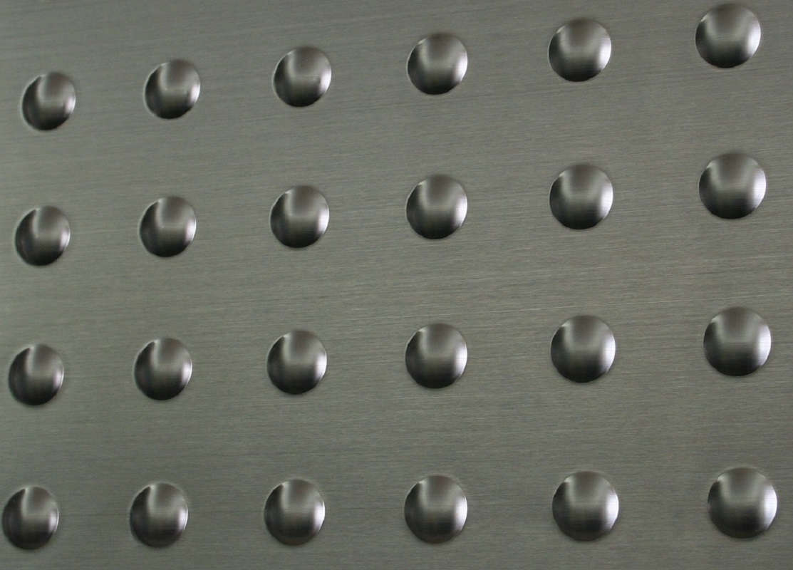 Close-up of a brushed metal surface with evenly spaced, circular, raised bumps arranged in a grid pattern.