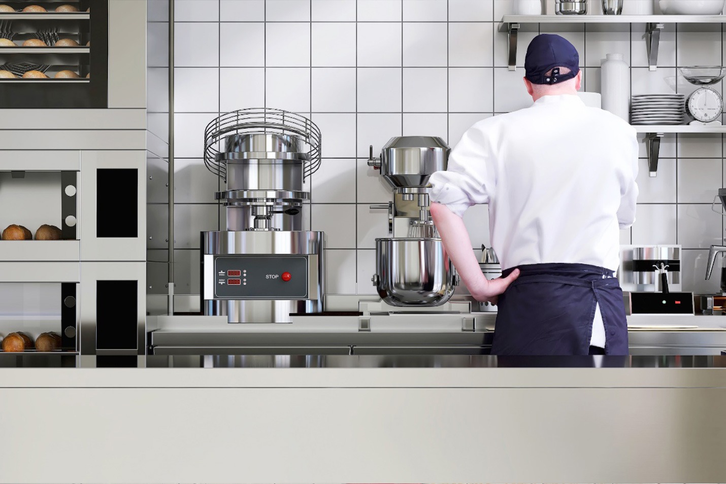A baker in a white uniform and navy cap stands in a modern bakery kitchen, facing industrial mixers and ovens, with shelves of bread and kitchen tools visible in the background.